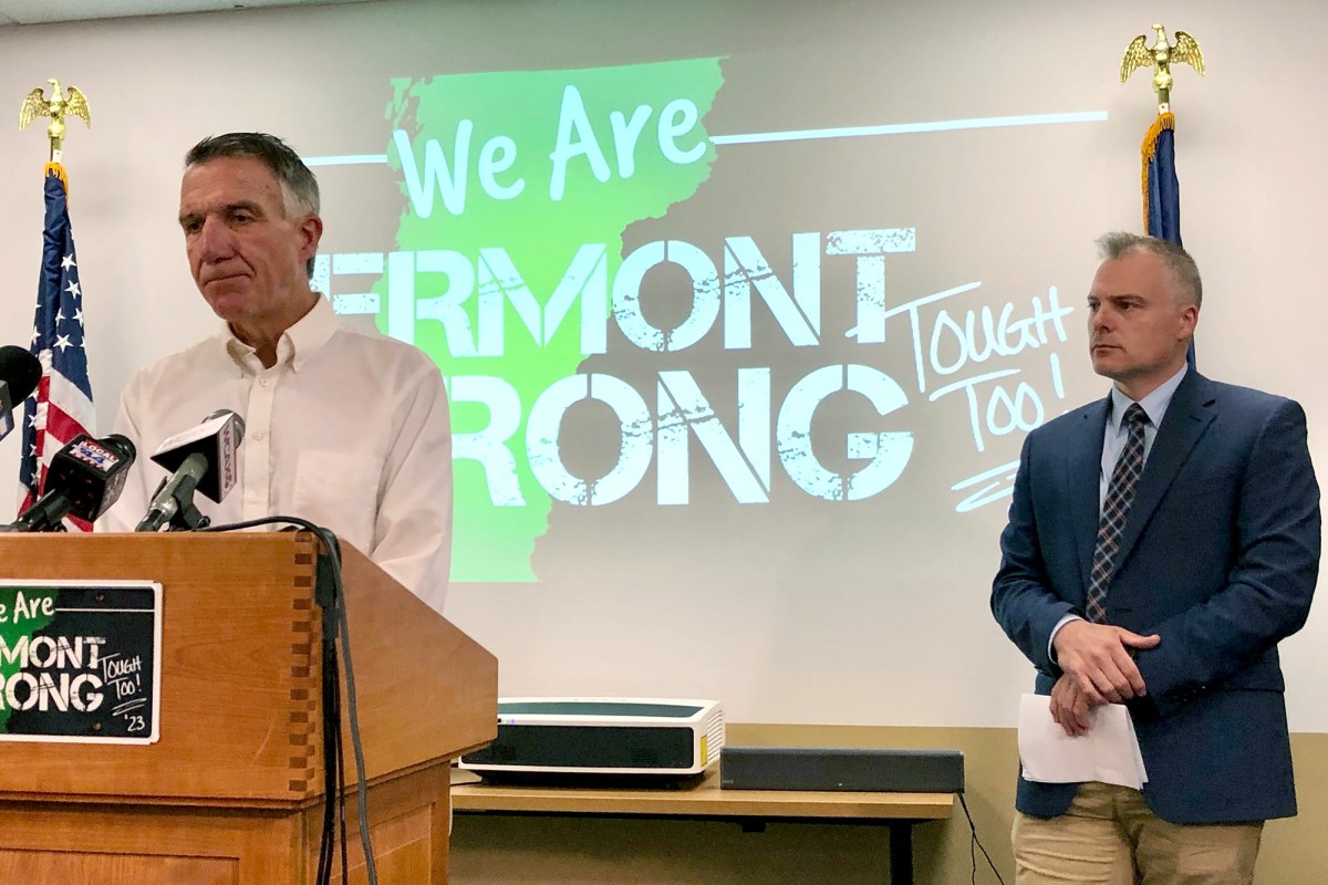 Two men stand in front of a projector that reads "We are Vermont Strong."