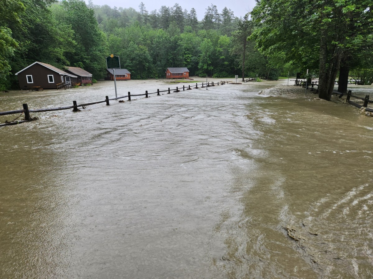 Floodwaters submerge a field and road in a rural area.