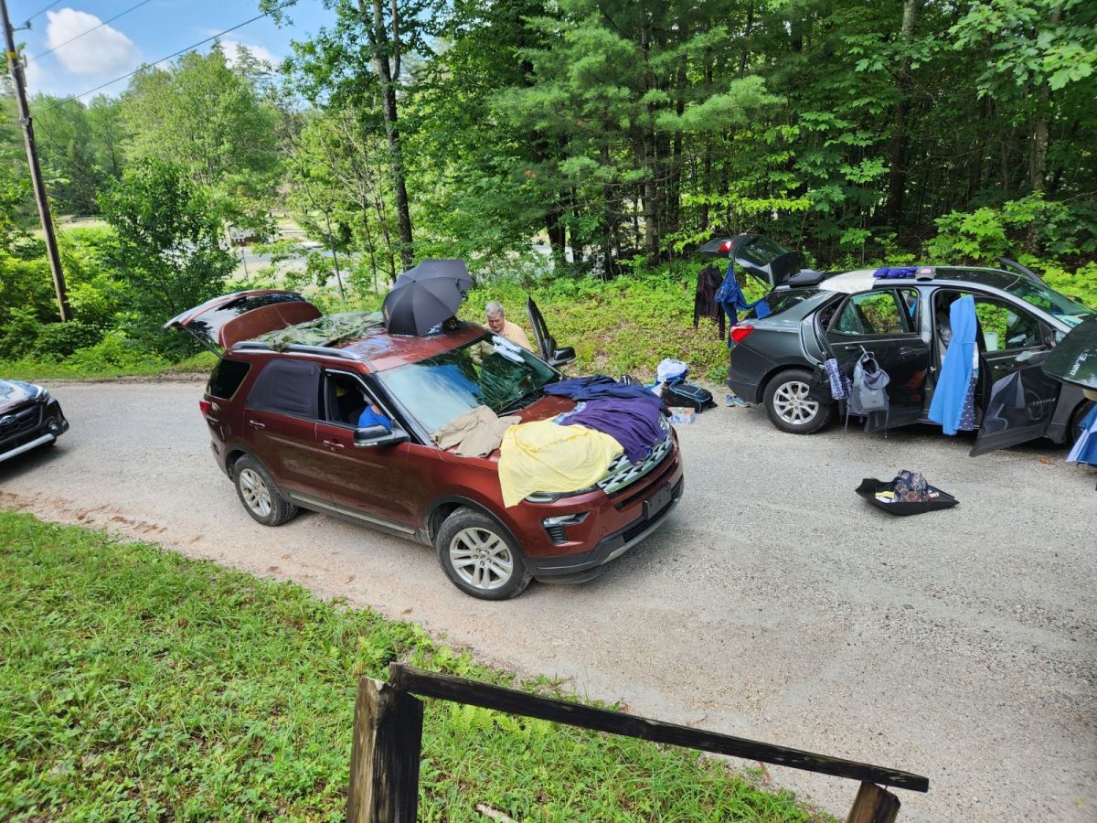 Cars with items drying on them on a dirt road in a rural area.