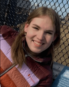 A woman in a maroon, purple, orange and red striped jacket.