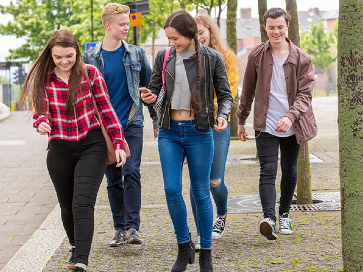 A group of young people walking down a sidewalk.
