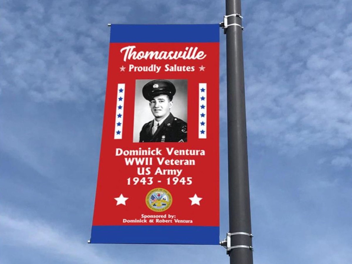 A banner honoring wwii veteran dominick ventura, displayed on a lamppost against a blue sky.