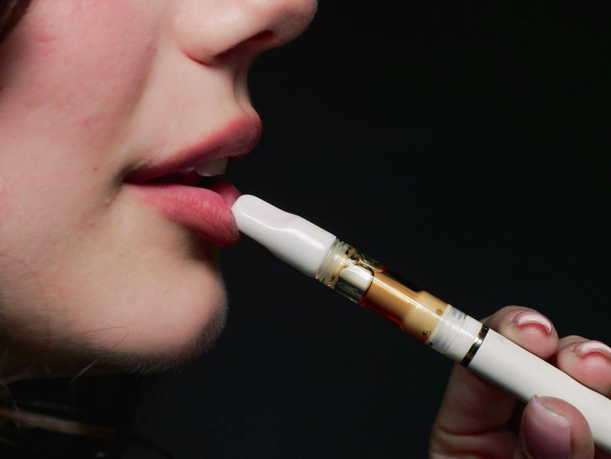 A young person holds an e-cigarette to their mouth.