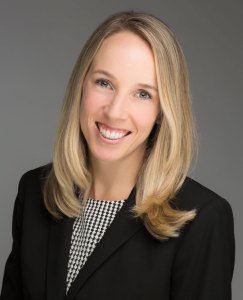 Professional headshot of a smiling woman with long blonde hair wearing business attire.