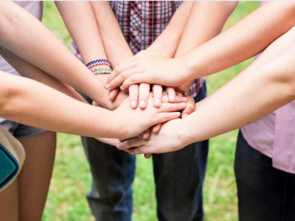A group of people with diverse hands stacked together in a gesture of teamwork and unity, standing outdoors.