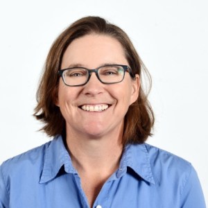 A woman in a blue button down standing in front of a white background.