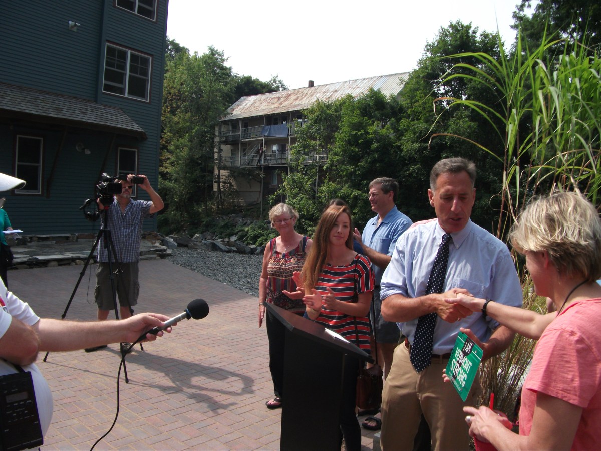 A man in a tie shakes someone's hand at an outdoor podium. 