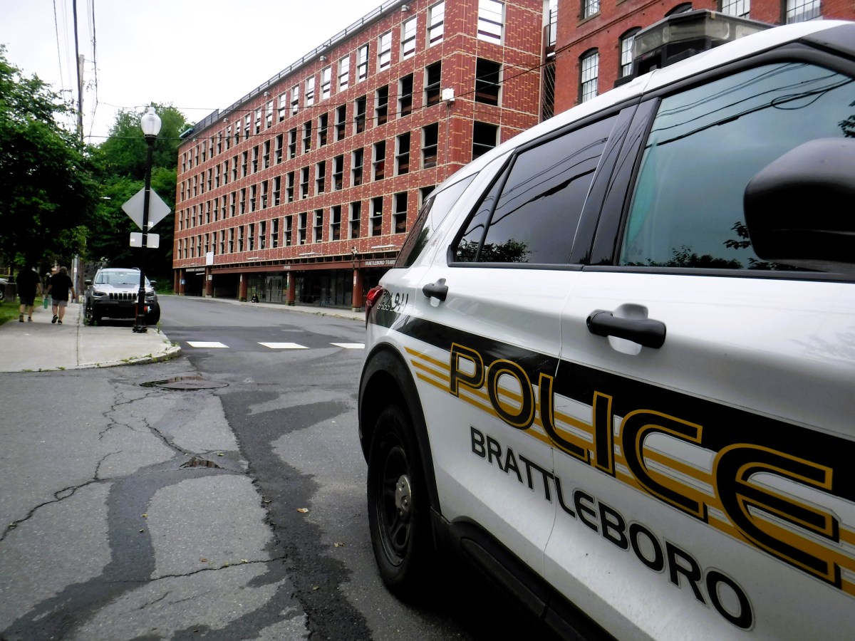 A police car labeled "Brattleboro Police" is parked on the street near a brick building.