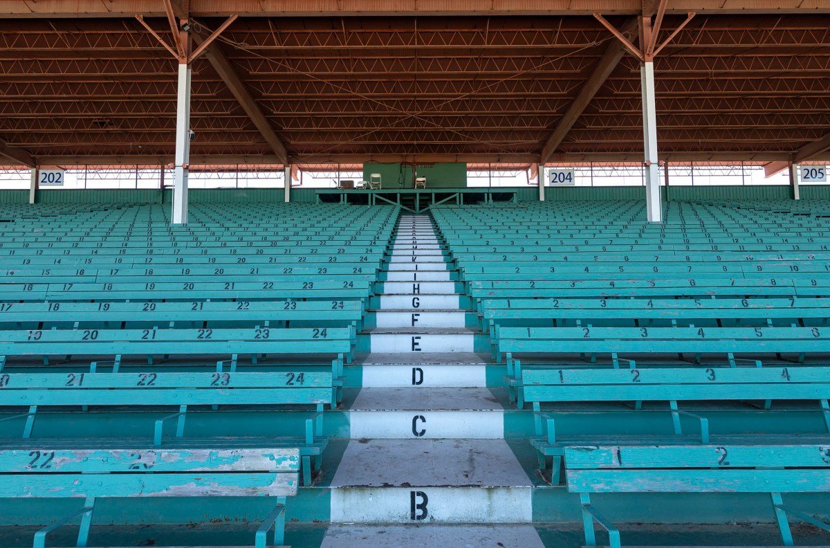 Empty green bleachers with numbered seats, labeled rows, stairs in the center labeled A to H, and section numbers 202, 204, and 205 under a large wooden roof.
