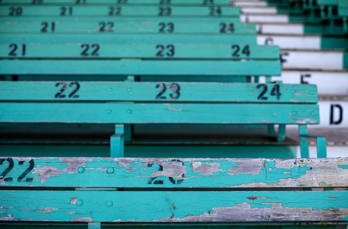 A worn-out wooden bench in section 23 of a stadium, with faded green paint and visible seat numbers.