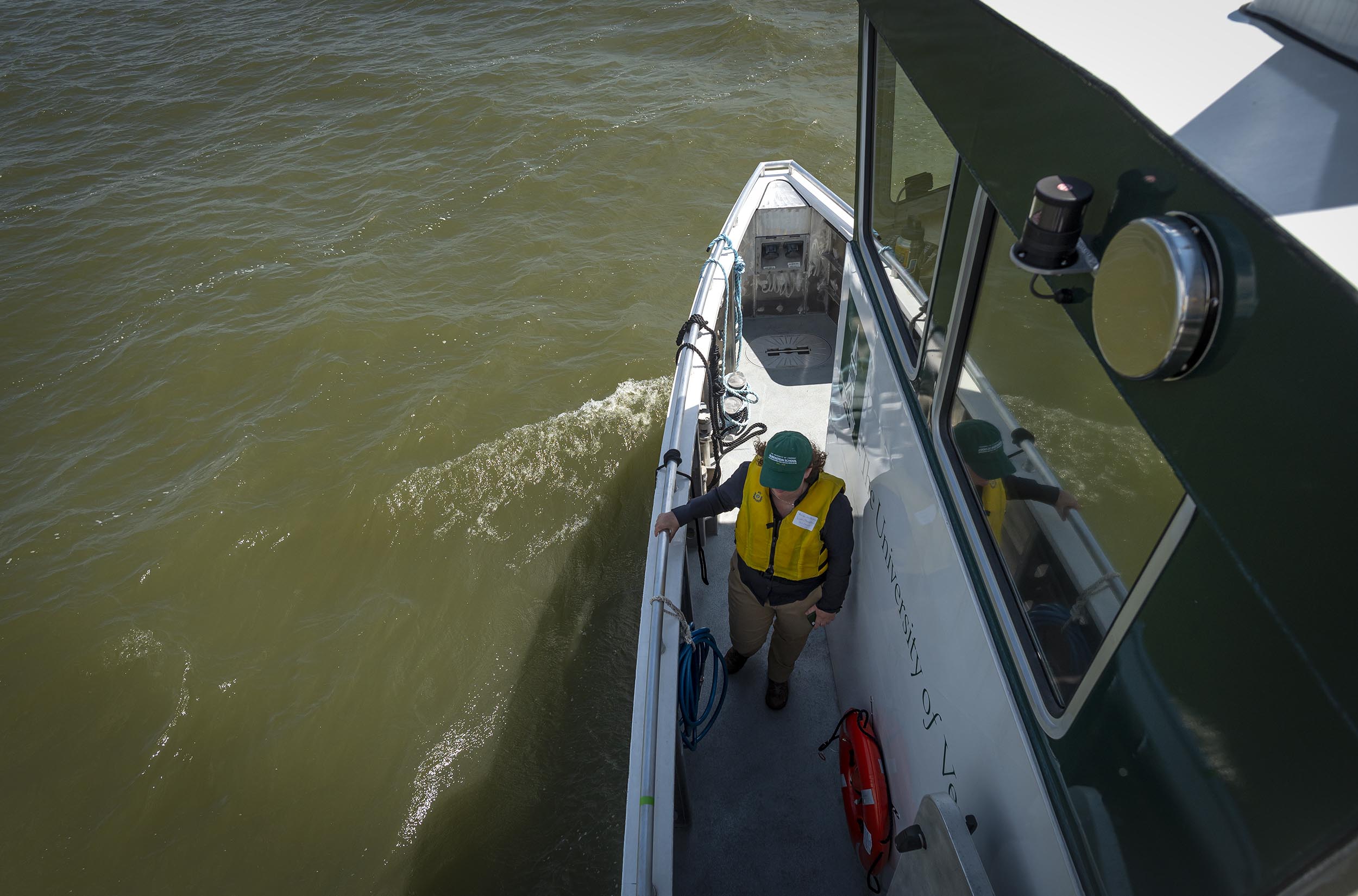 A person wearing a yellow life jacket stands on the deck of a boat near the railing, with the boat partially submerged in water.