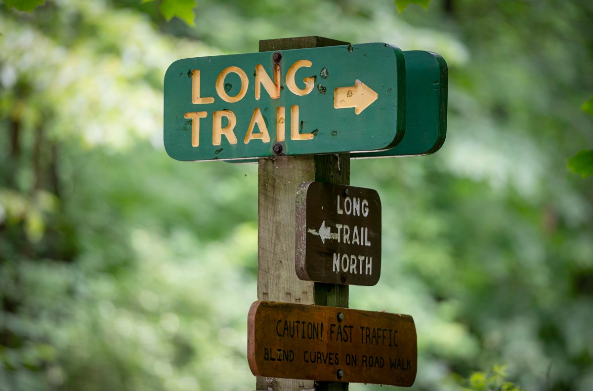 Signpost in a wooded area indicating directions for the Long Trail and Long Trail North, with a caution about fast traffic on the road walk.