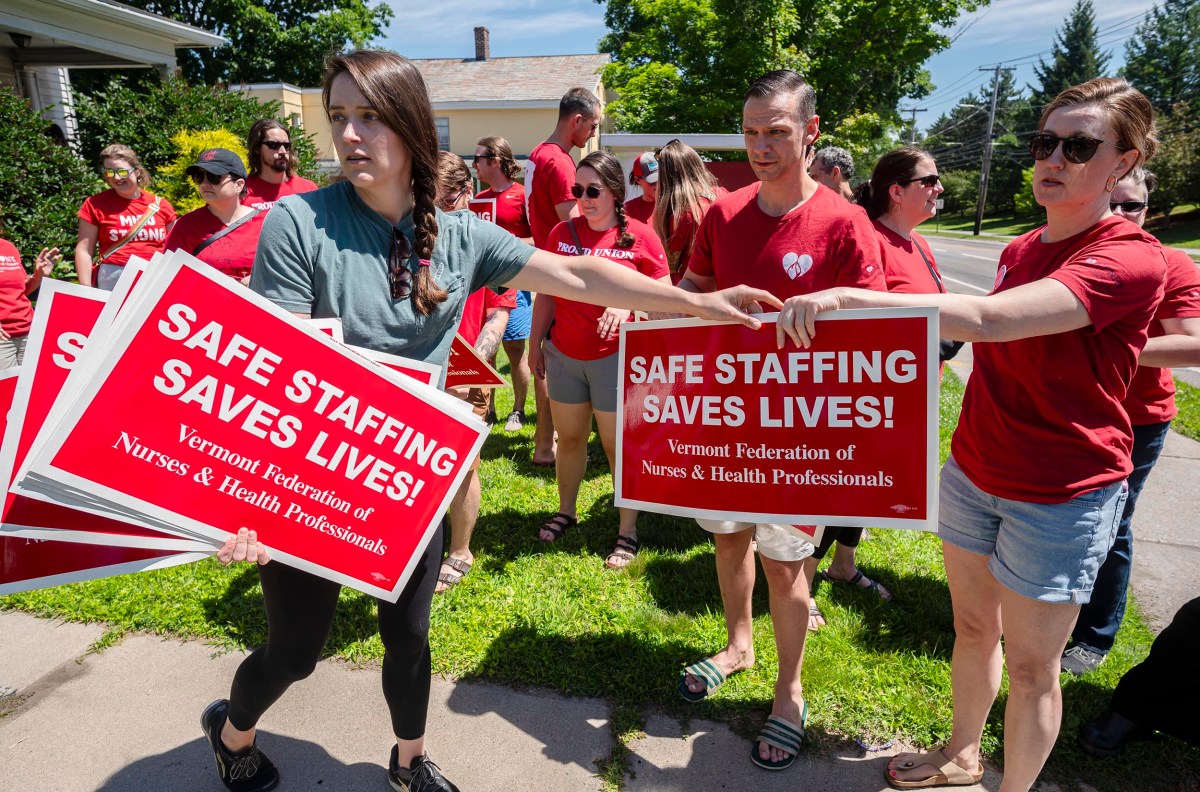 People in red shirts gather while holding signs that say "Safe Staffing Saves Lives!" from the Vermont Federation of Nurses & Health Professionals.