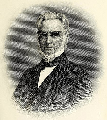 A grayscale portrait of an older man with glasses, white hair, and mutton chops, wearing a suit with a bow tie.