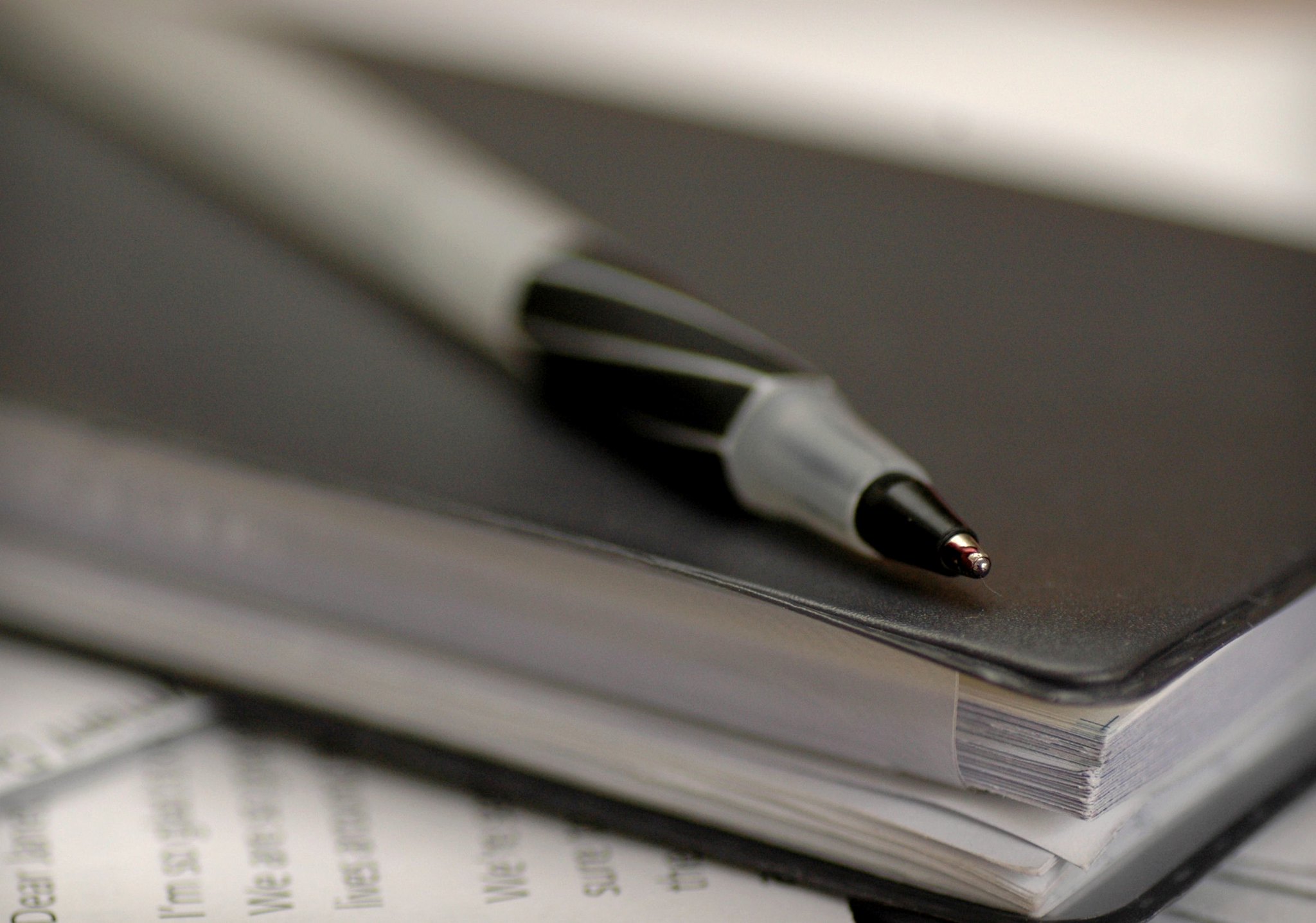 A black pen rests on a closed black notebook placed on top of scattered papers.