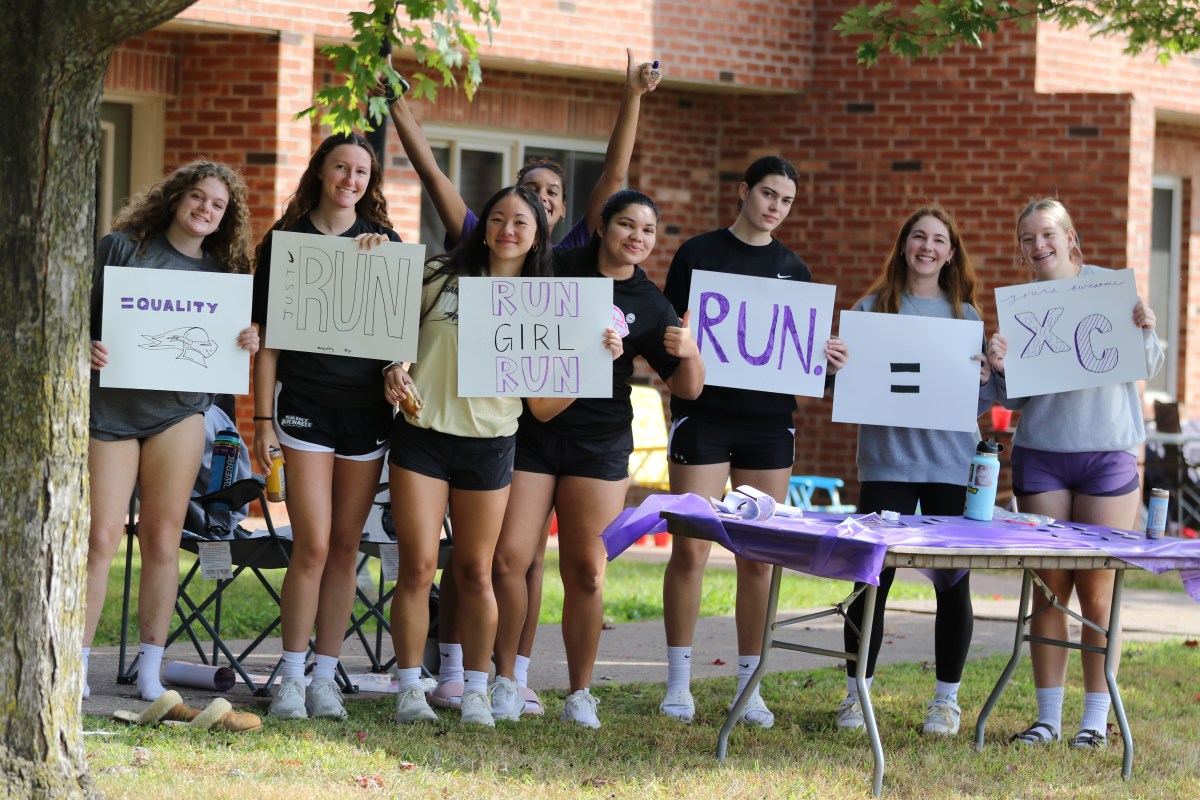 A group of people holding signs promoting running stand together outdoors beside a table.