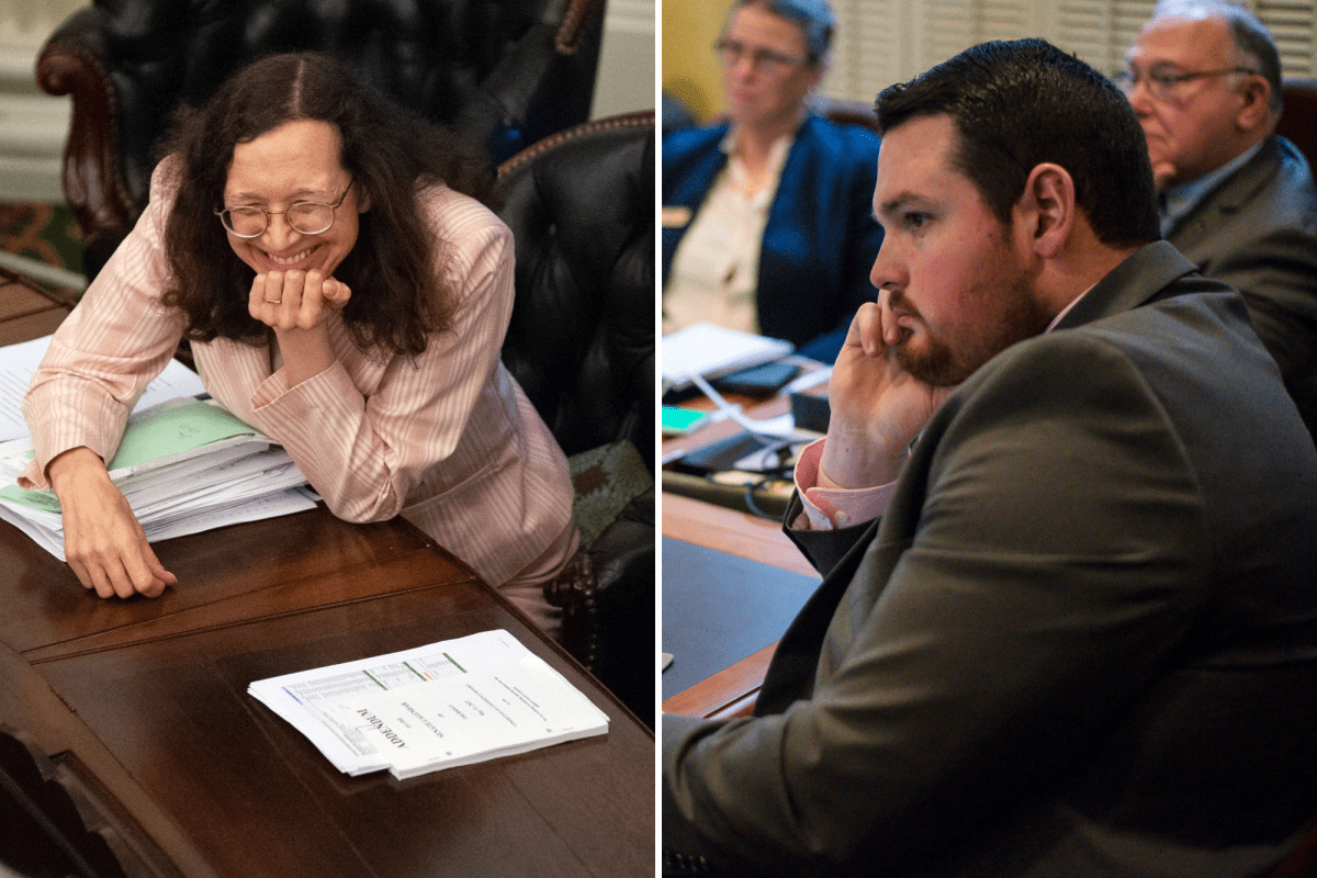 Two people seated in a meeting room. One woman smiles with papers on the table; the man on the right listens thoughtfully with his hand on his chin. Others are in the background.
