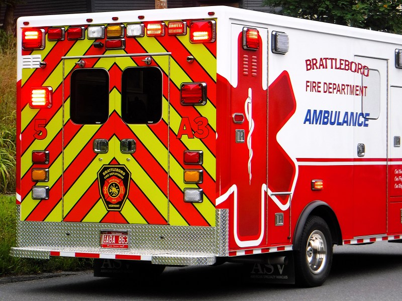 Rear view of a Brattleboro Fire Department ambulance with red and yellow chevron stripes, emergency lights, and department insignia.