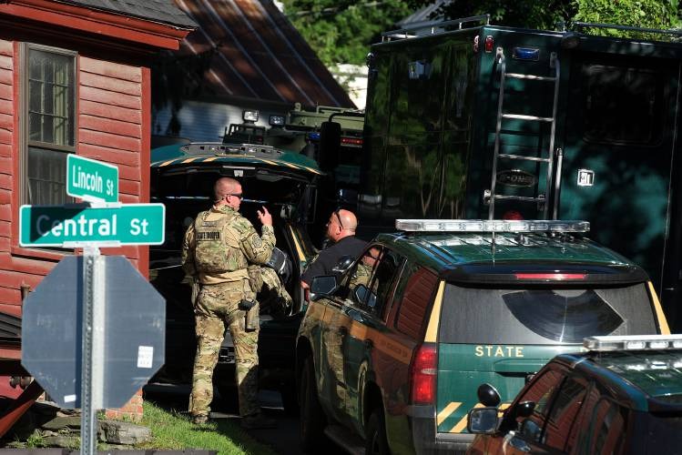 Law enforcement officers in tactical gear stand near parked vehicles at an intersection with Lincoln St and Central St signage visible.