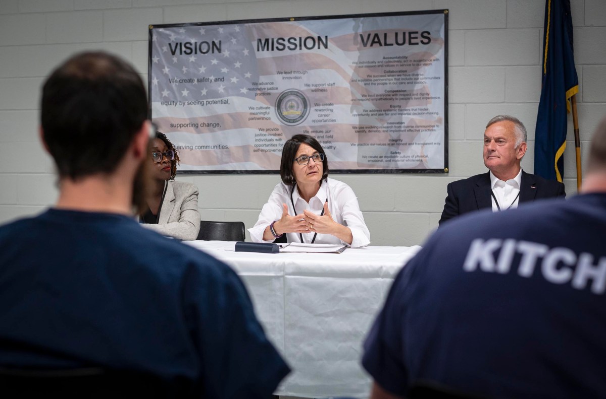 A panel of three people sits at a table in front of an audience. A "Vision, Mission, Values" poster is in the background.