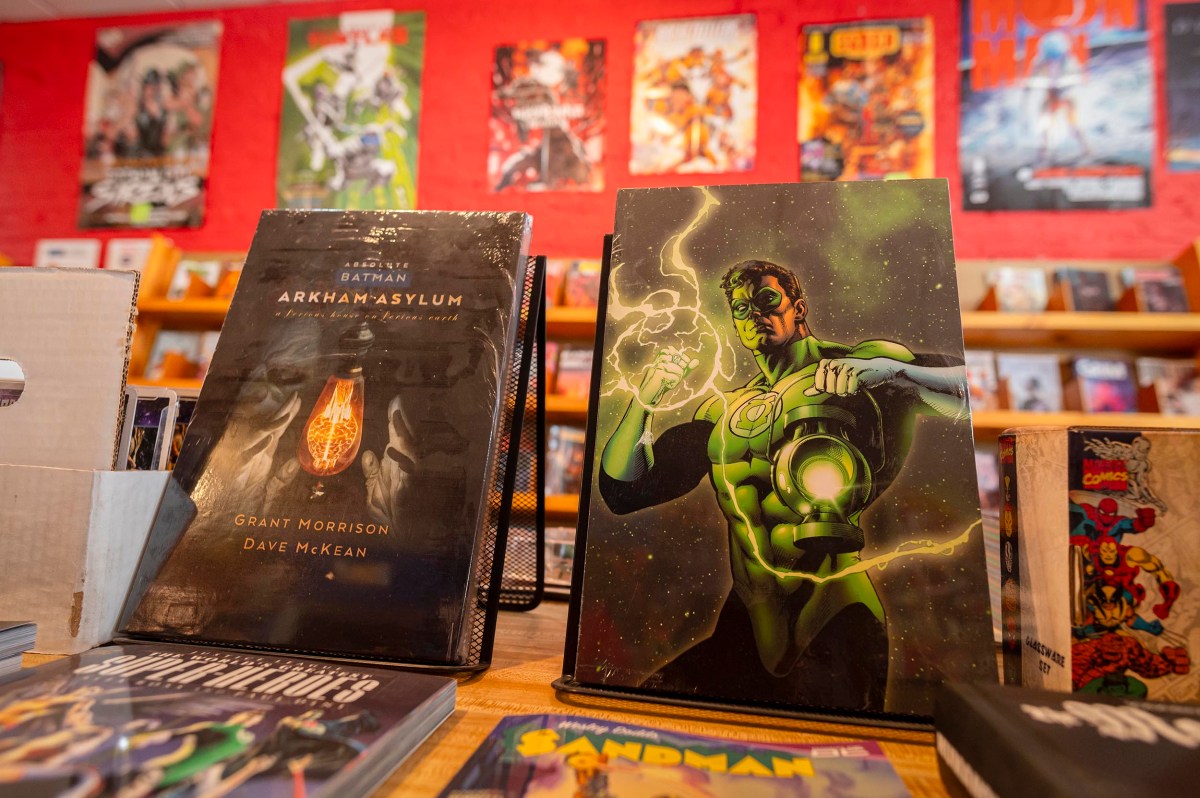 A comic book store display featuring "Batman: Arkham Asylum" and a Green Lantern comic book, with more comics and posters in the background.