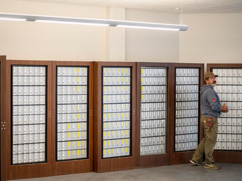 A man walks past rows of locked mailboxes in a post office.