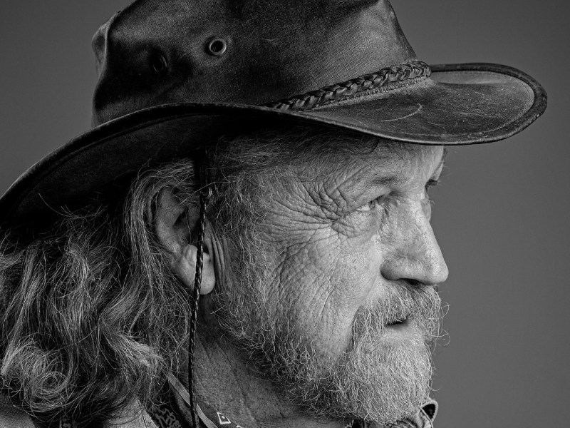 Black and white side profile of an older man with a beard, wearing a wide-brimmed leather hat and looking into the distance.