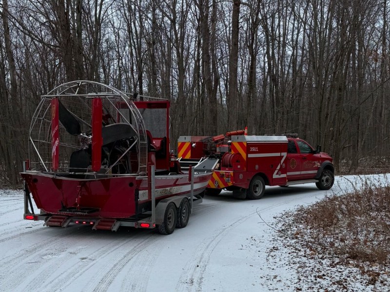 A red fire rescue truck tows a boat on a snowy forest road.