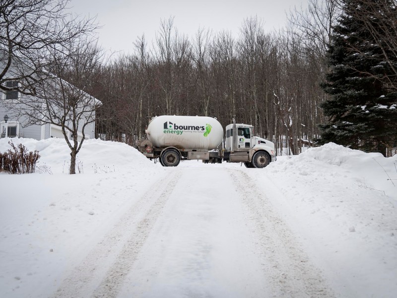 A truck labeled "Bourne's Energy" is parked on a snow-covered driveway next to a house, surrounded by snowbanks and trees.