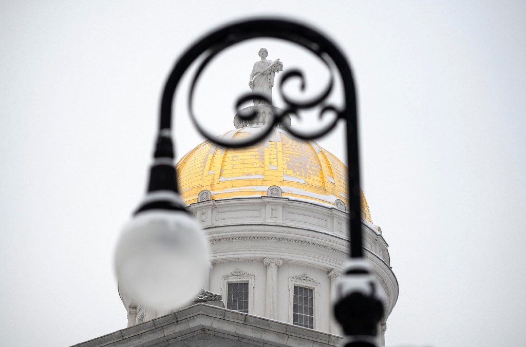 A golden-domed building with a statue on top is partially obscured by a black ornate streetlamp, set against a gray sky.