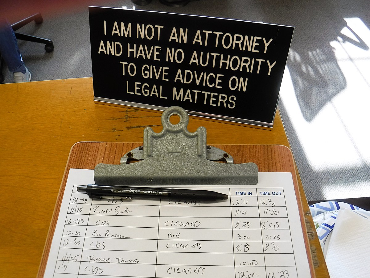 Sign on a desk reads: "I am not an attorney and have no authority to give advice on legal matters," with a clipboard and pen lying on a table below.