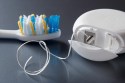 A toothbrush with blue and yellow bristles is next to an open container of dental floss on a gray surface.