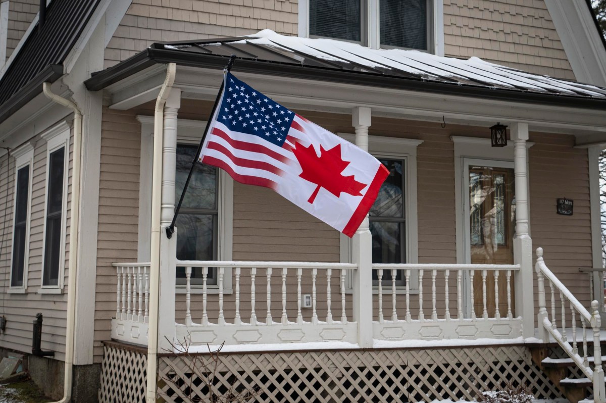 A house with a porch features a flag combining elements of the U.S. and Canadian flags.