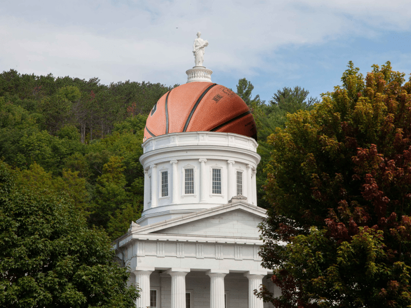 A classical white building with a dome resembling a basketball, surrounded by green trees under a partly cloudy sky.