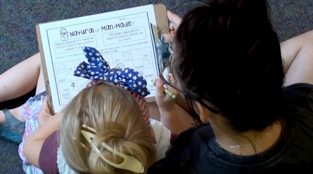 Child with a star-patterned bow and adult working on a "Natural or Man-Made?" worksheet on a clipboard.