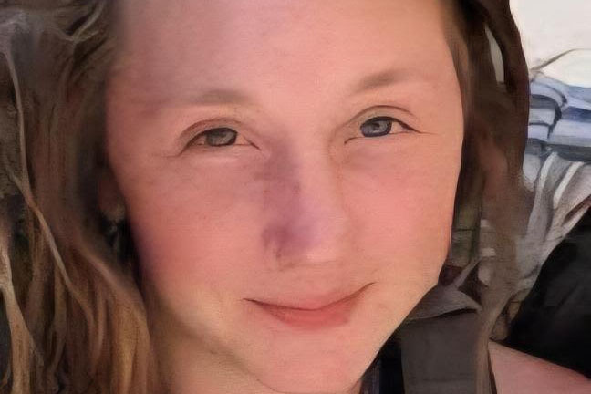 A person with light skin and long brown hair looks at the camera, smiling softly. The background is out of focus.