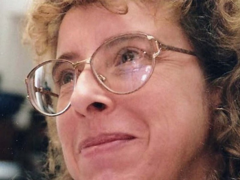 A person with curly hair, glasses, and a slight smile, seen in a close-up shot.