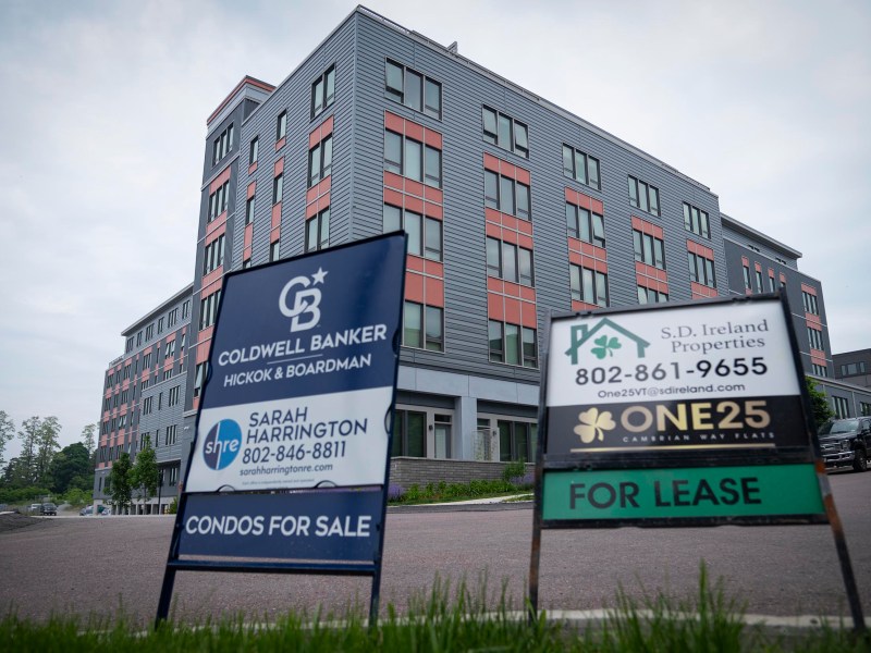 A modern apartment building with "Condos for Sale" and "For Lease" real estate signs displayed on the lawn in front.