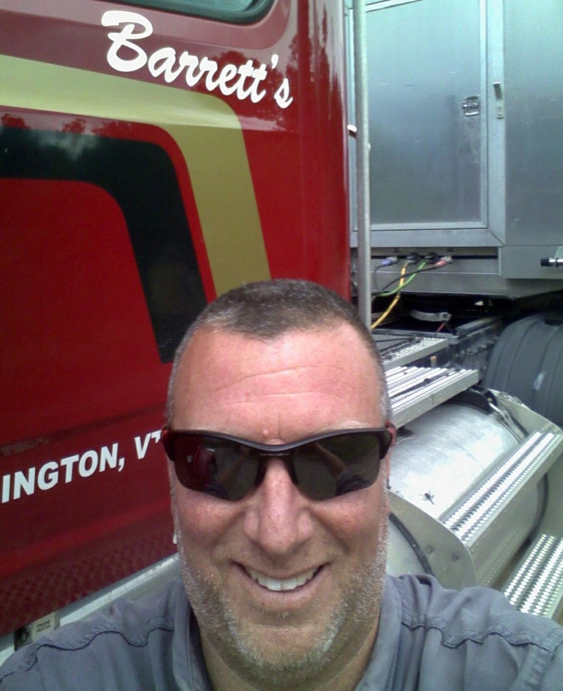 A man wearing sunglasses smiles in front of a red truck with "Barrett's" written on it.