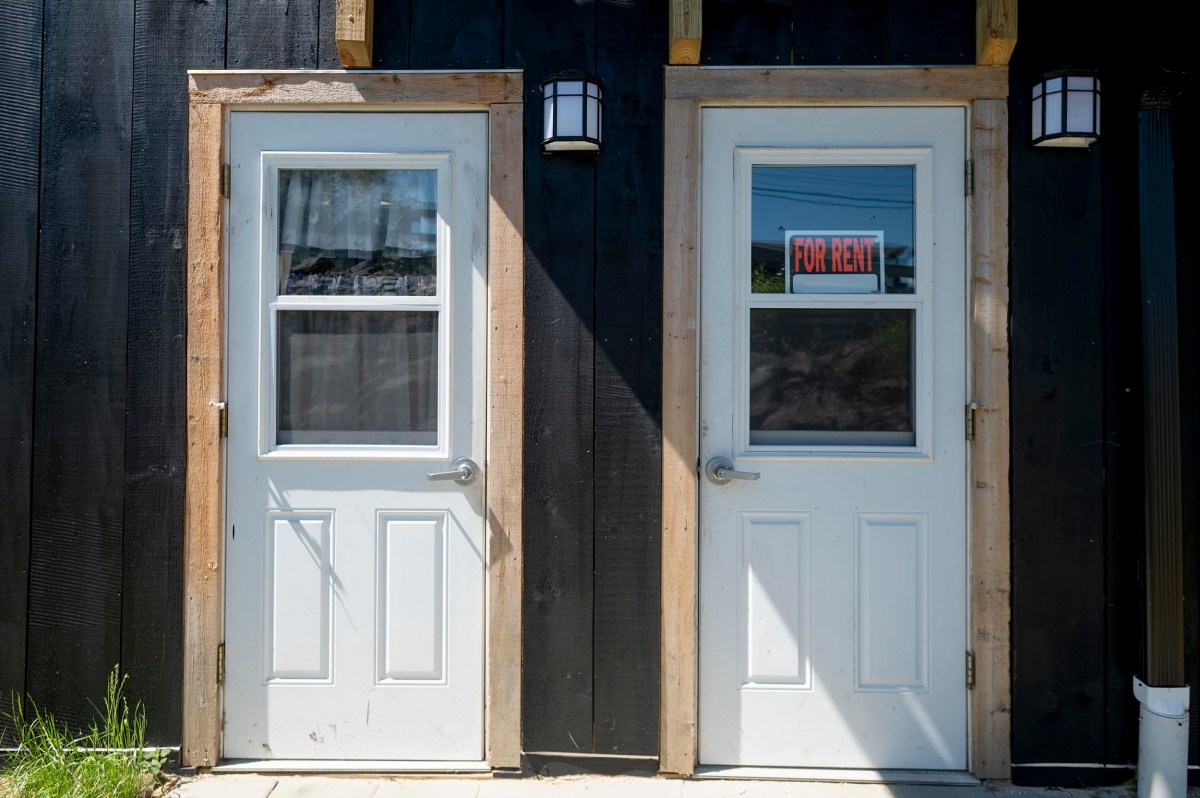 Two white doors on a black building; the door on the right has a "For Rent" sign in its window.