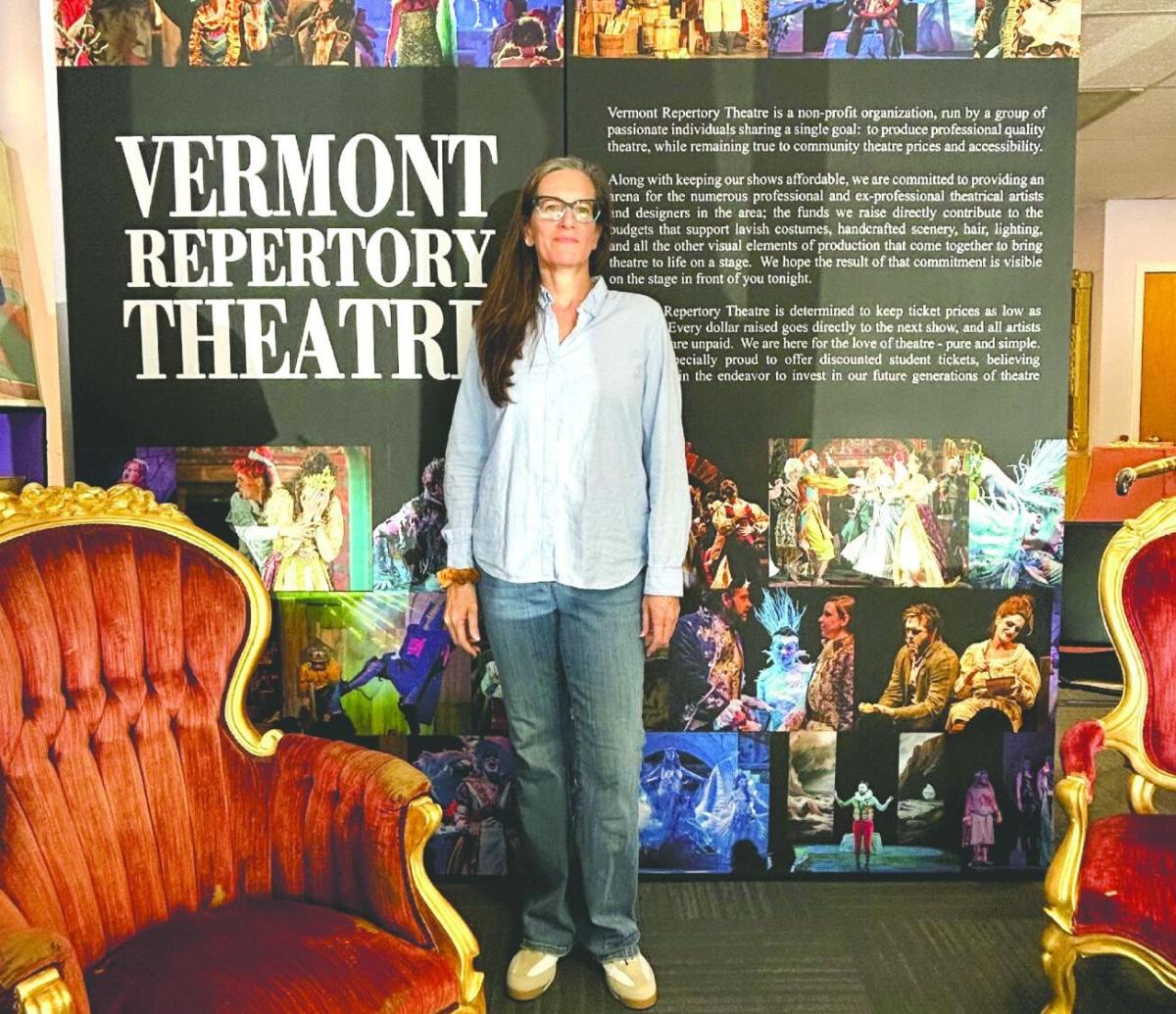 A woman stands in front of a Vermont Repertory Theatre display, flanked by ornate chairs, with images and text about the theatre in the background.