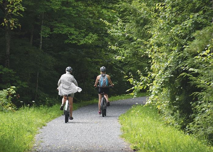 Two people wearing helmets ride bicycles on a gravel path through a lush green forest.