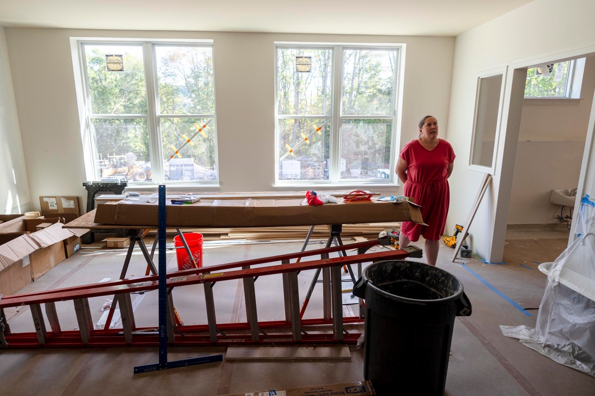 A woman in a pink dress stands in a room under construction with large windows, tools, boxes, and ladders scattered on the floor.