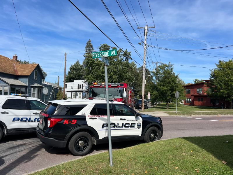 Police vehicles and a fire truck are parked near a street intersection with a visible "Riverside Ave" sign on a clear day.