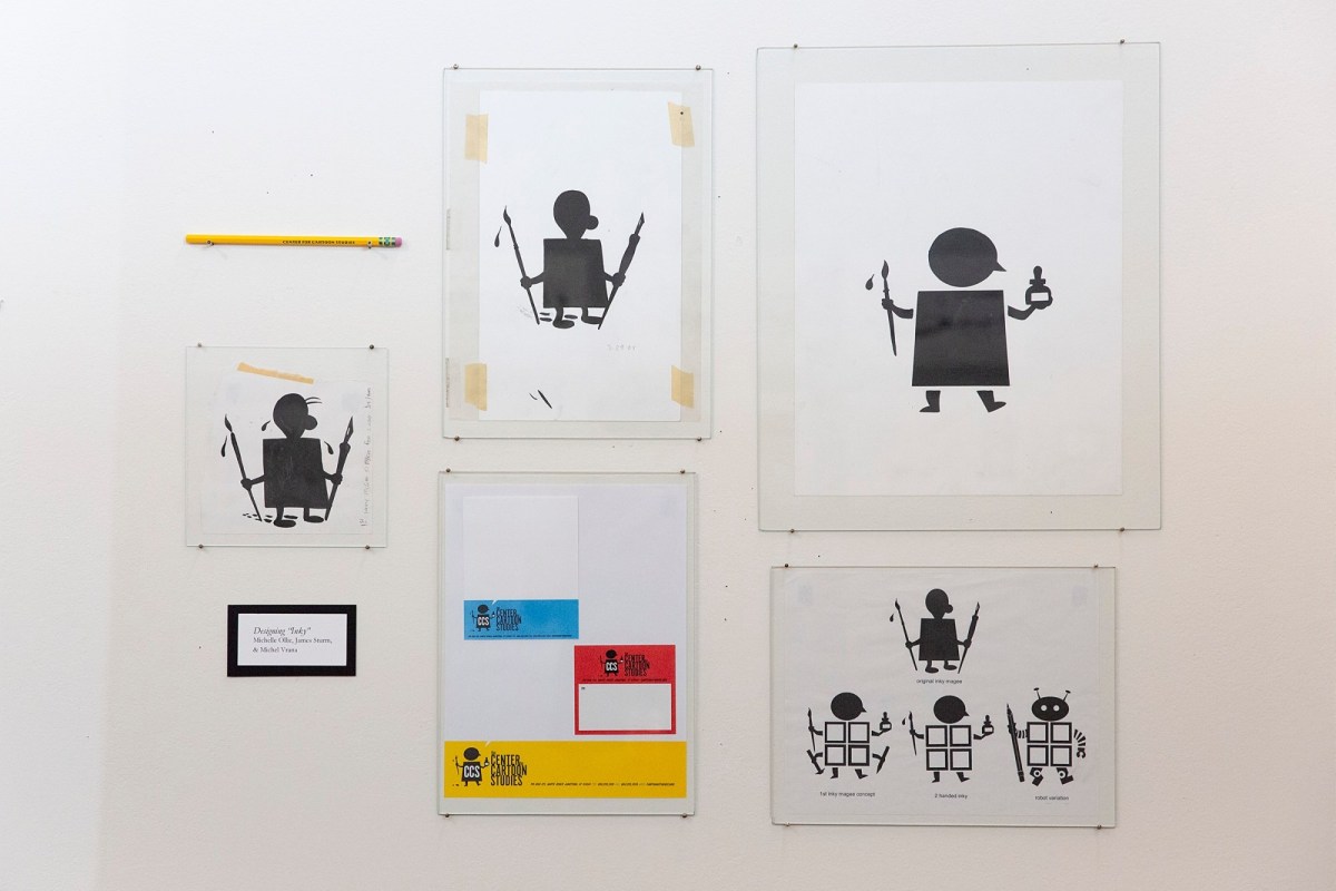 Various framed prints of simple black robot-like figures are displayed on a white wall, along with a pencil and a colorful print at the bottom center.