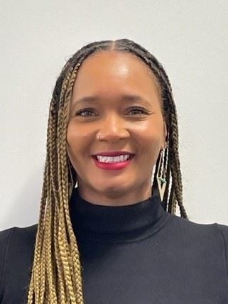 A woman with long braided hair, wearing a black turtleneck top and geometric earrings, smiles at the camera against a plain light background.