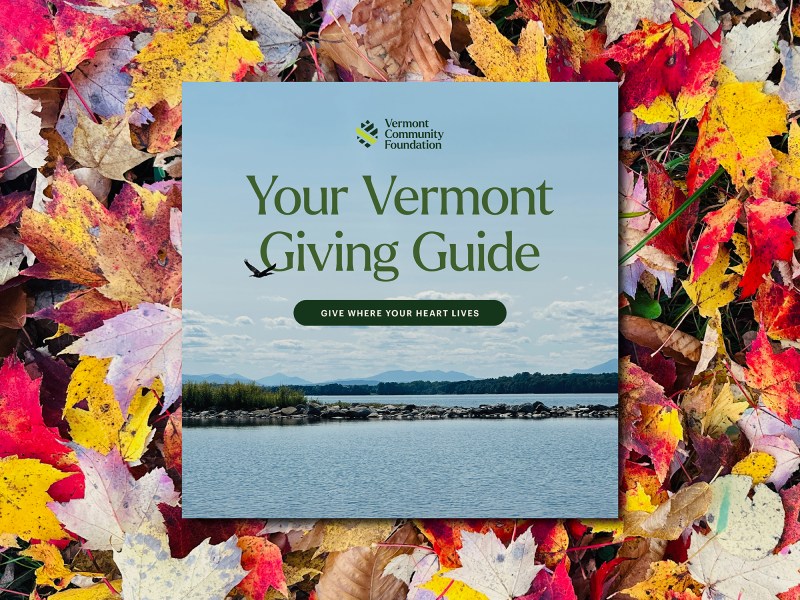A booklet titled "Your Vermont Giving Guide" lies on colorful autumn leaves; the cover features a lake scene and the Vermont Community Foundation logo.