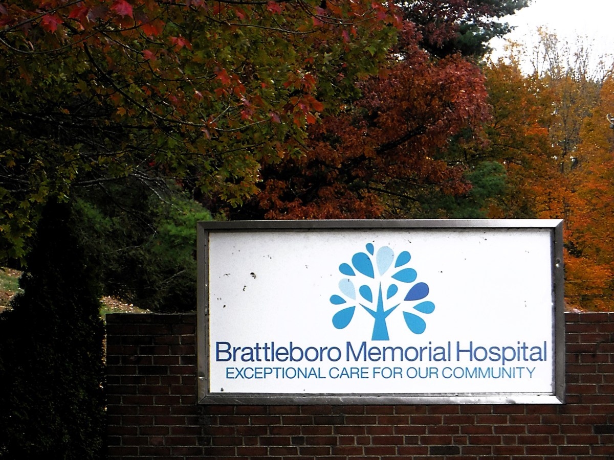 Sign for Brattleboro Memorial Hospital, featuring a blue tree logo and the slogan "Exceptional care for our community," with autumn trees in the background.