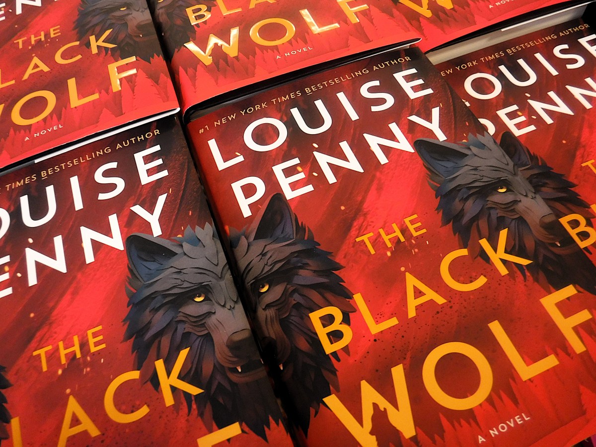 Multiple copies of the book "The Black Wolf" by Louise Penny are arranged in a pattern; the cover features a dark wolf illustration on a red background.