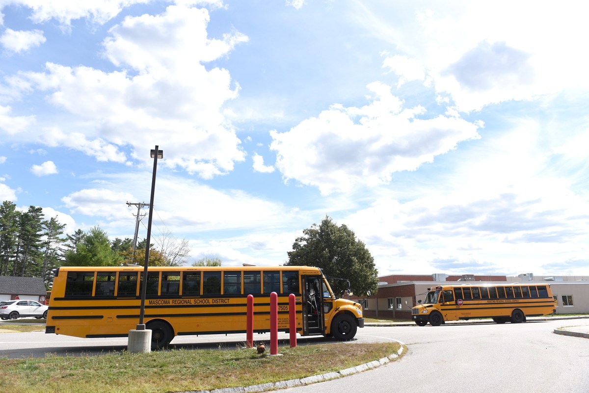 Two yellow school buses are parked outside a school building under a partly cloudy sky.